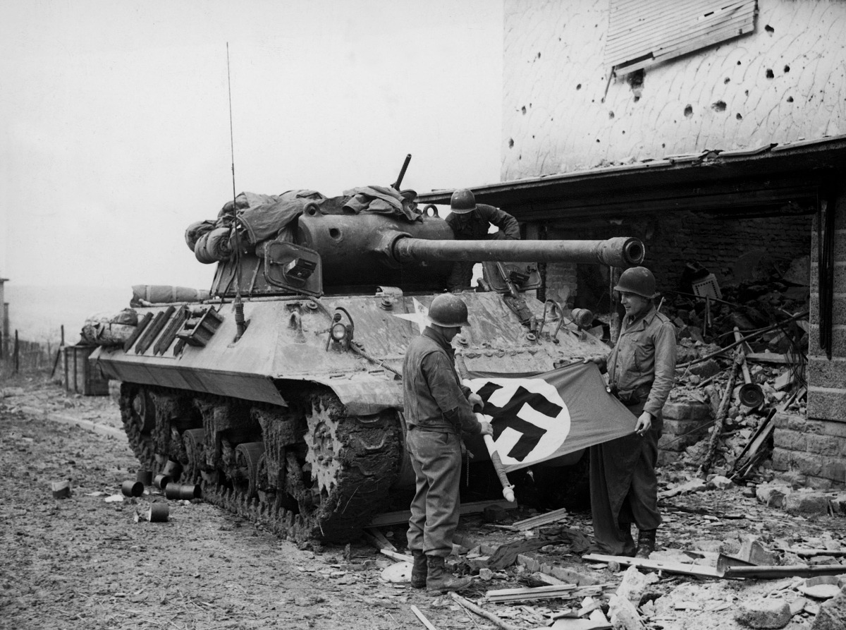 American soldiers of Patton's Third Army standing in front of their M36 TD while rolling up a Nazi flag they have taken as a trophy after the capture of Bitberg.